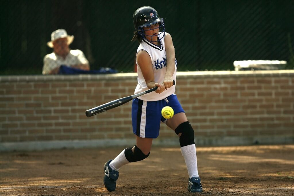 Woman in White Sleeveless Jersey Holding a Black Baseball Bat Pitching the Green Tennis Ball